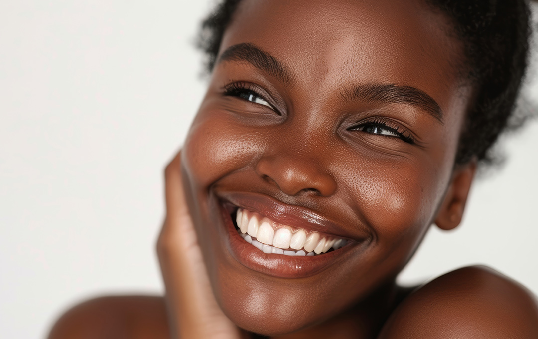 Woman smiling with clear, glowing skin after a luxurious facial tailored to her skin’s needs for cleansing, exfoliation, and hydration.