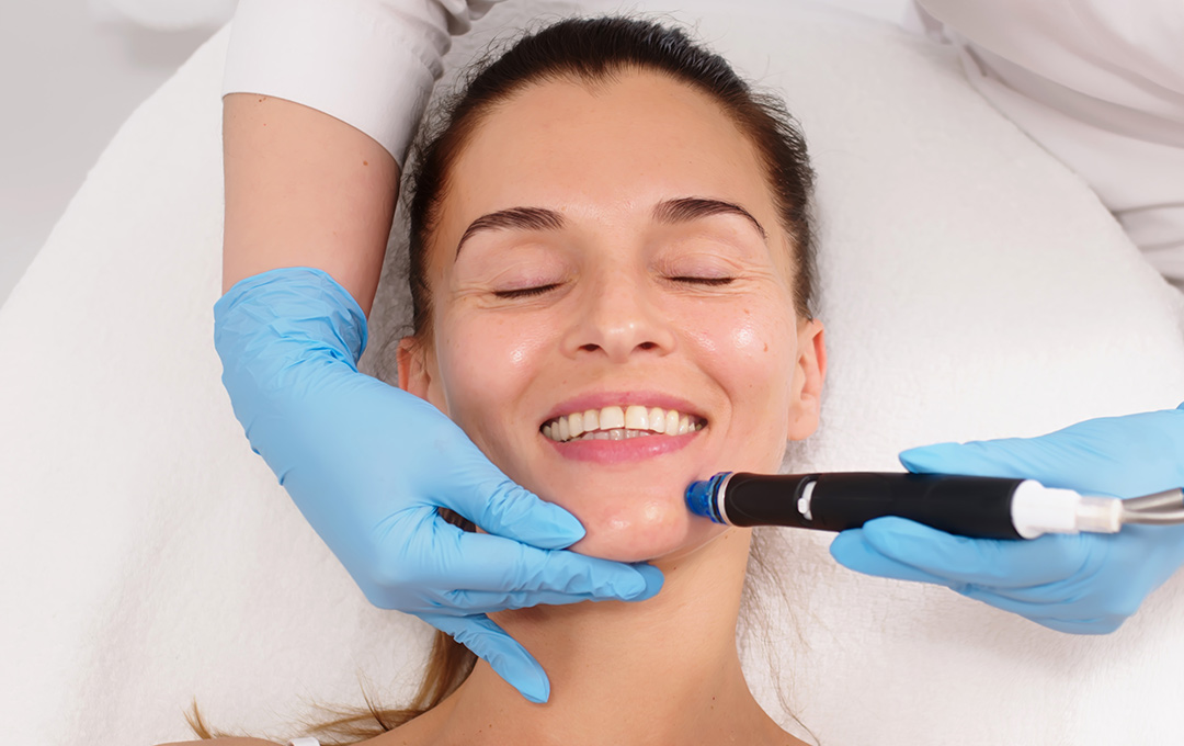 Woman smiling while receiving a Hydrafacial, an all-in-one treatment for cleansing, exfoliation, and hydration with immediate results.