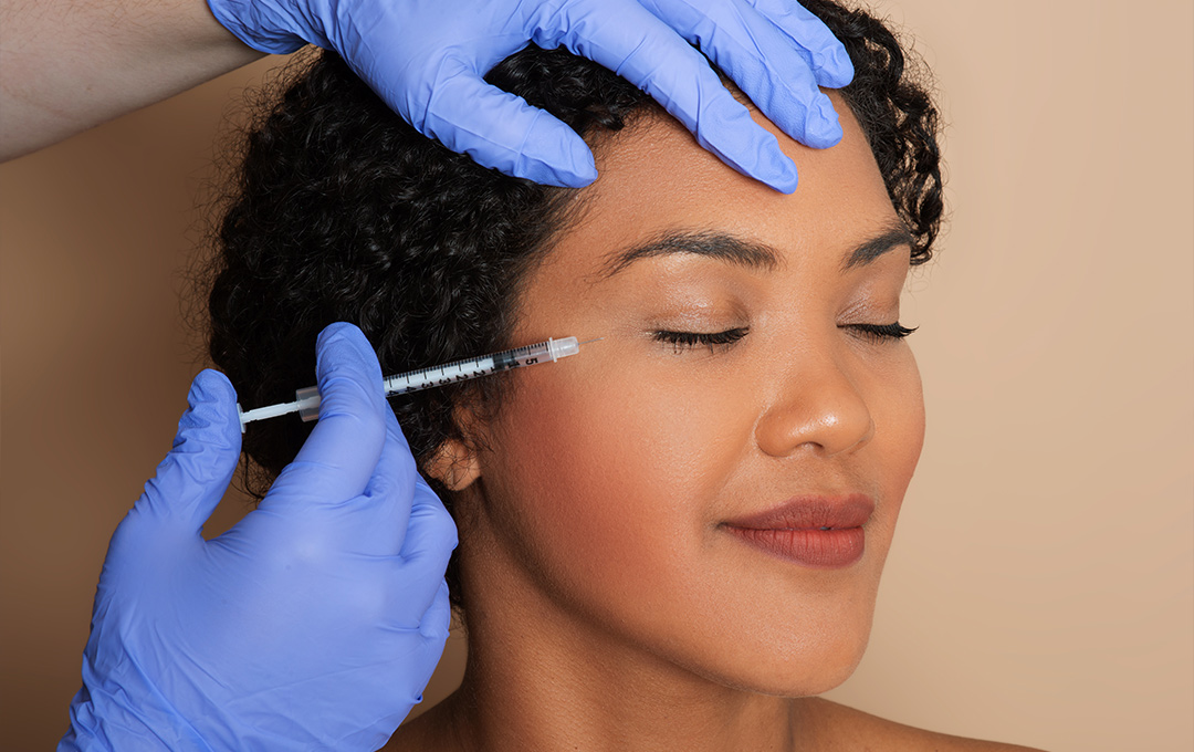 Woman with her eyes closed, smiling, receiving a Botox injection around her eyes to reduce wrinkles.